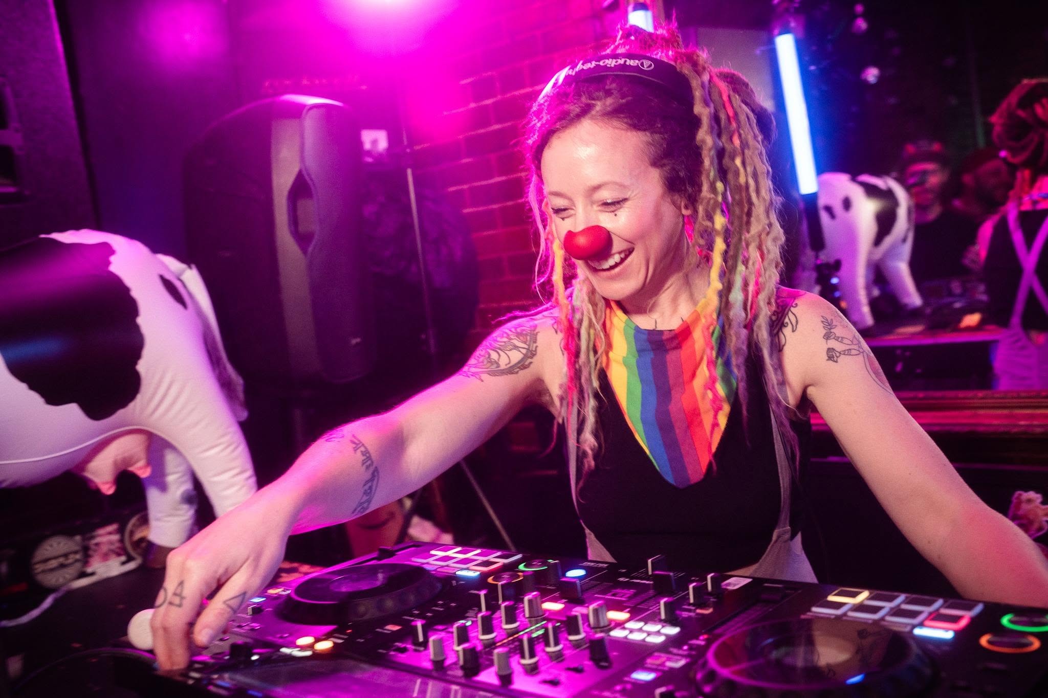 Amelia DJing under pink lights with a red clown nose